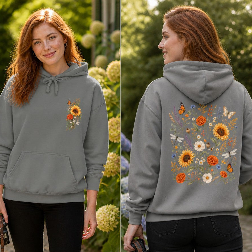 Woman wearing a grey boho sweatshirt decorated with a whimsical sunflower, butterfly, and wildflower floral design, photographed in a lush garden setting, perfect for nature-loving women, by Crossroads Dandelion