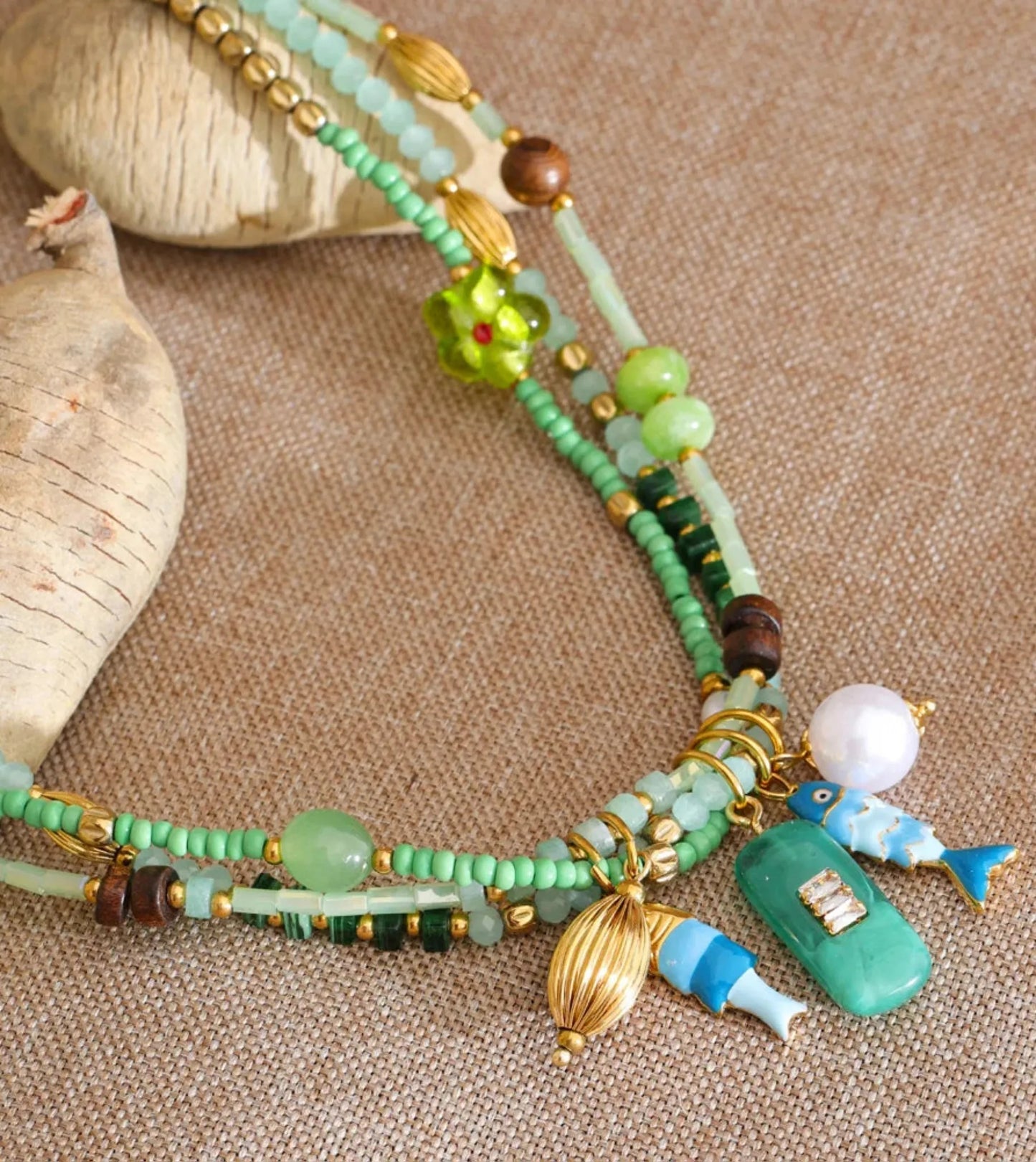 Colorful beaded necklace with fish and coastal charms on a textured surface by Crossroads Dandelion