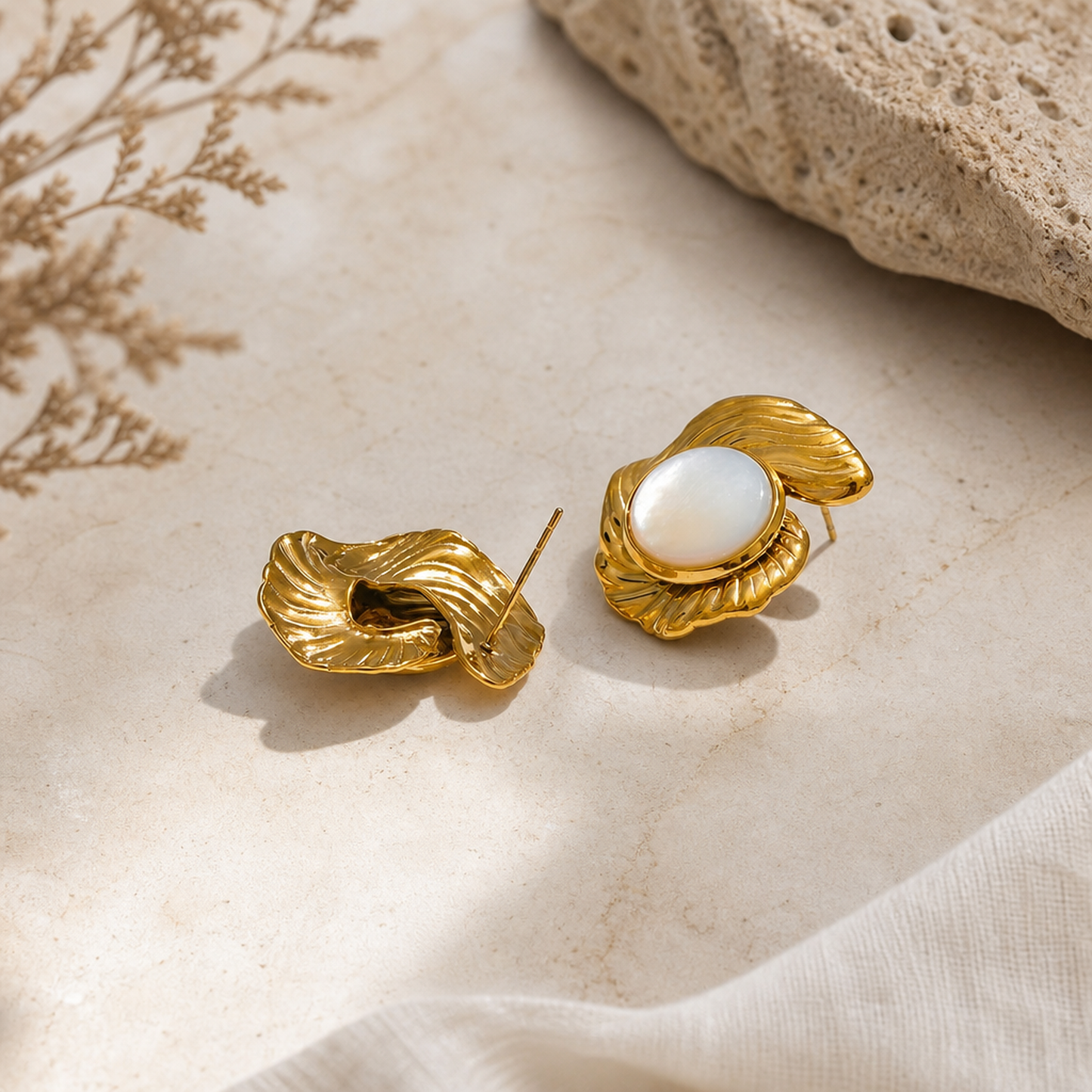 Elegant gold stud earrings with pearl detail displayed on marble surface with natural stone accents, product photography, by Crossroads Dandelion