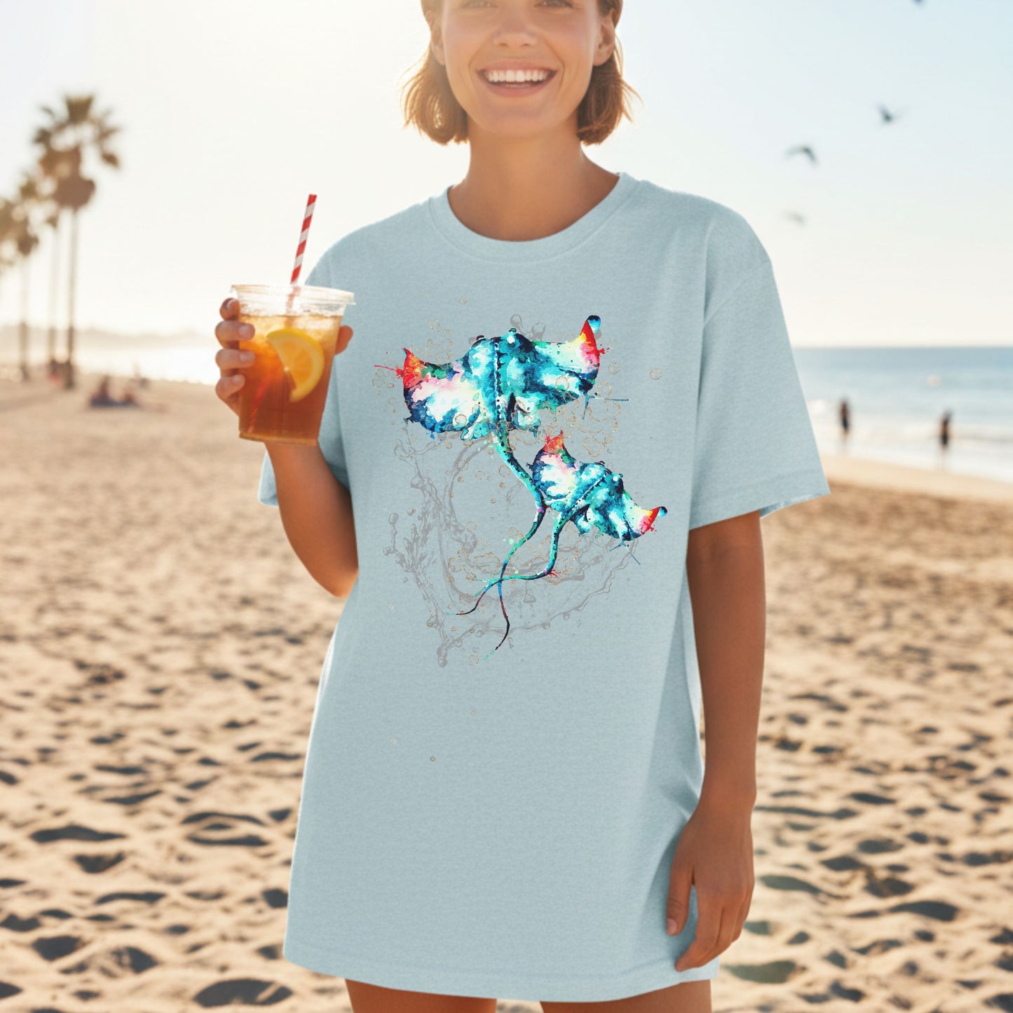 Woman wearing a heather ice blue t-shirt with a colorful stingray design on a beach.