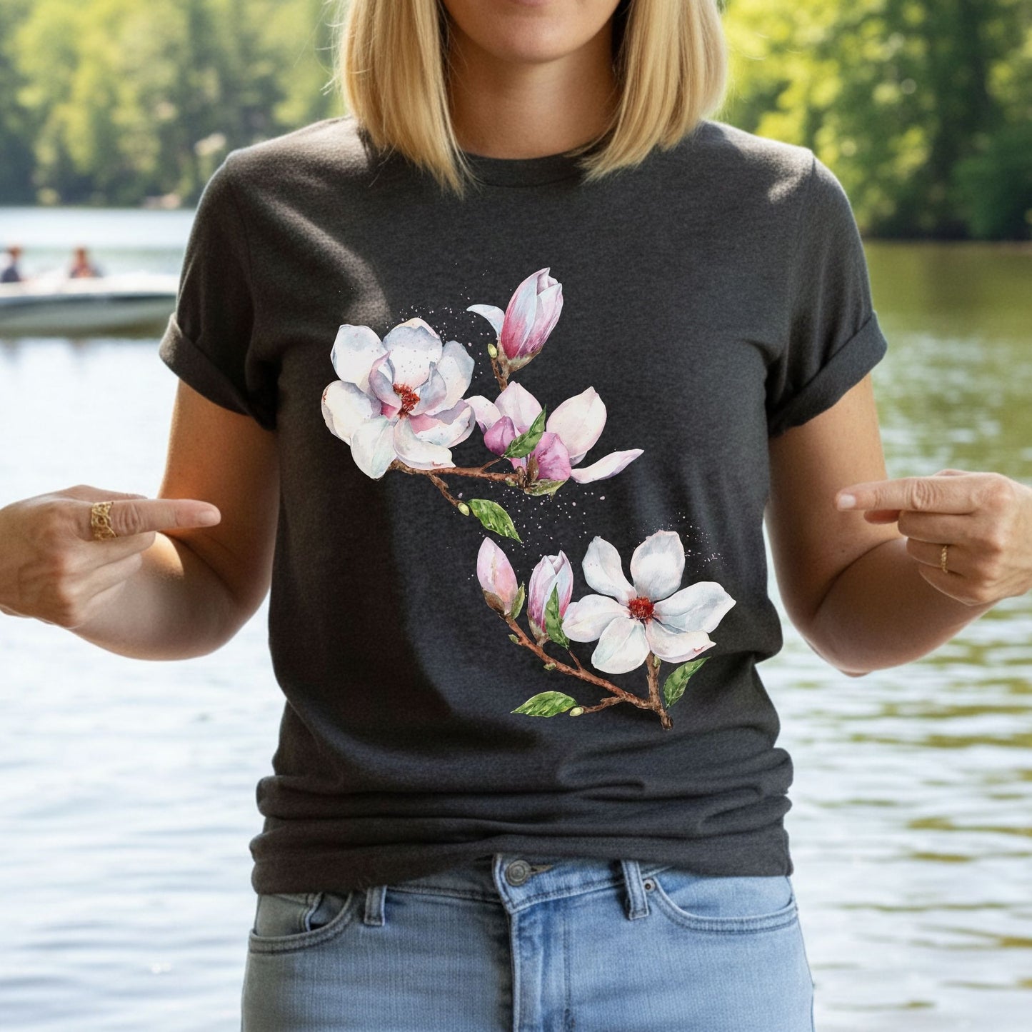 Woman wearing a dark gray heather magnolia flower tee with watercolor botanical floral design by a lake by Crossroads Dandelion