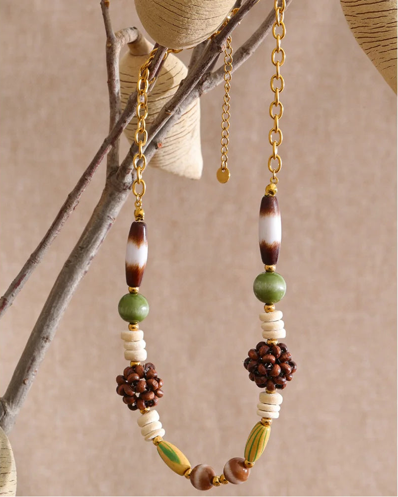 Beaded necklace with brown, green, and white beads on a branch against a beige background