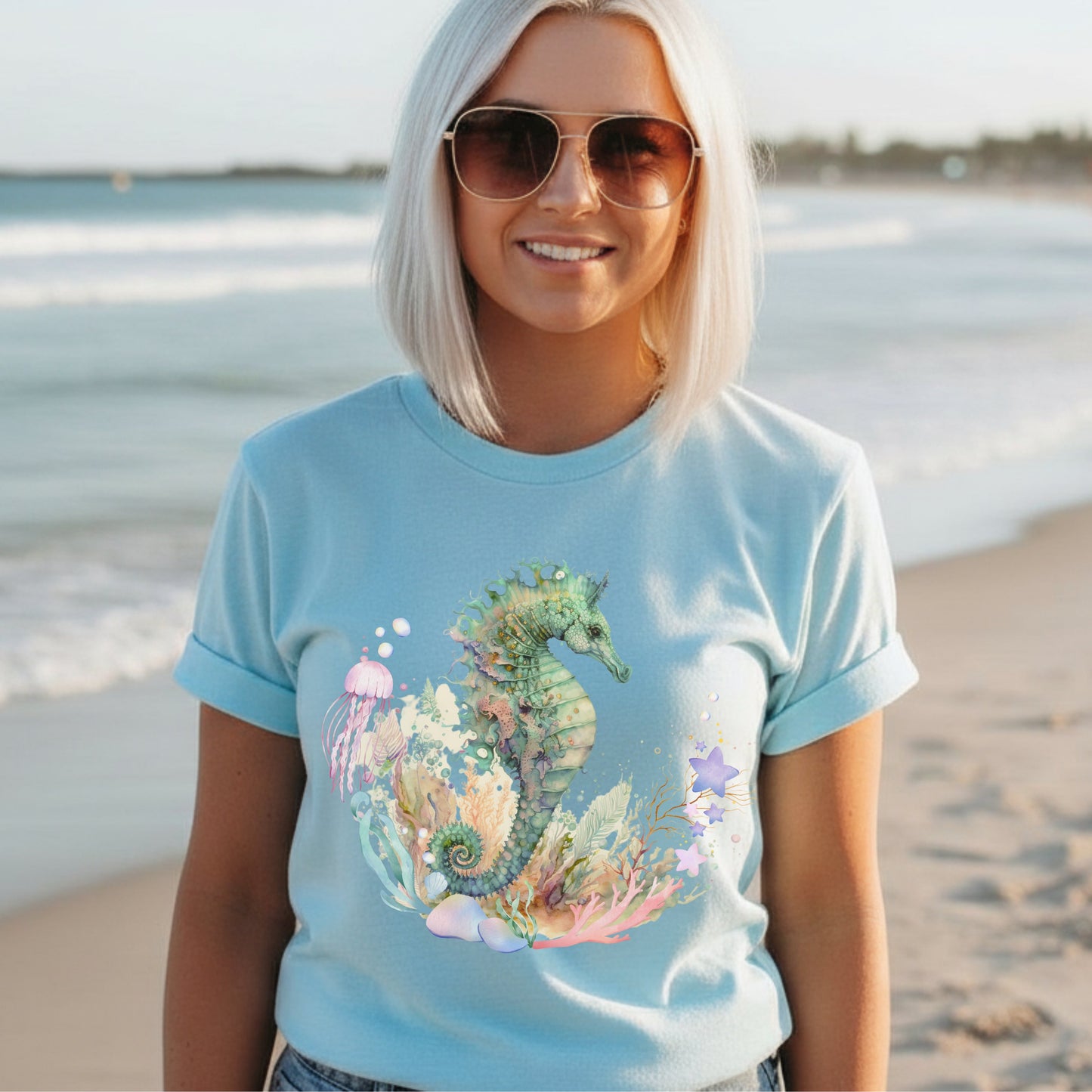 Woman wearing an Ocean seahorse shirt in heather ice blue, wearing glasses, by a beach