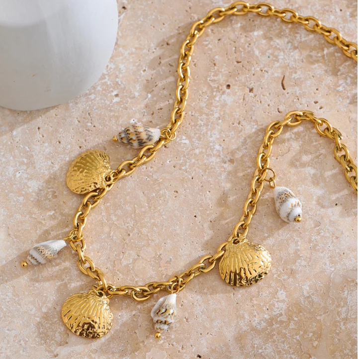 Gold bracelet with shell charms on a textured beige surface