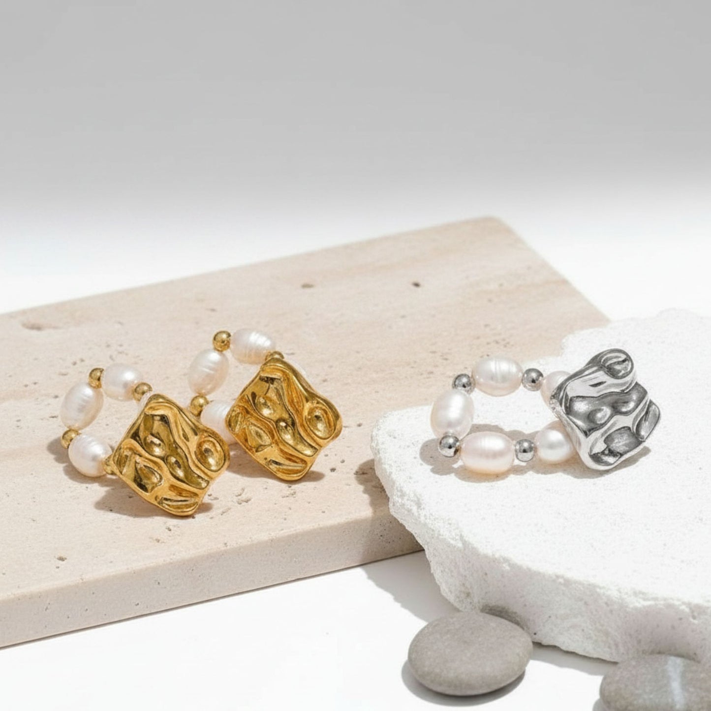 Baroque freshwater pearl hoop drop earrings in gold and silver PVD plated stainless steel, both colorways displayed on travertine marble surface with white stones, by Crossroads Dandelion
