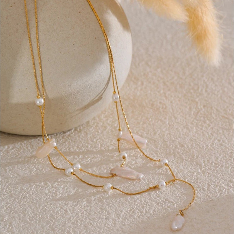 Baroque pearl layered necklace draped over a cream vase beside soft pampas grass