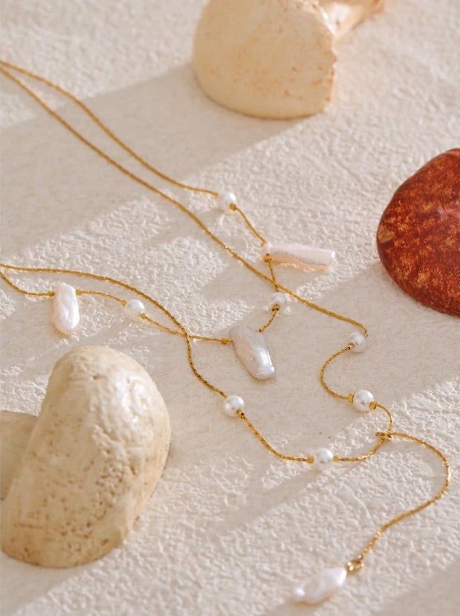 Baroque pearl layered necklace laid on textured cream plaster between smooth stones