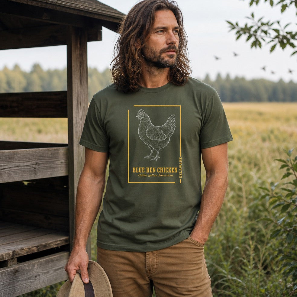Man wearing a military green Bella Canvas 3001 t-shirt featuring a vintage-style line art illustration of a Blue Hen Chicken with botanical hand-lettered text, evokes cottagecore nostalgia and state pride, standing by a rustic wooden shed in a serene meadow, perfect for birdwatchers, wildlife enthusiasts, and heritage lovers, by Crossroads Dandelion