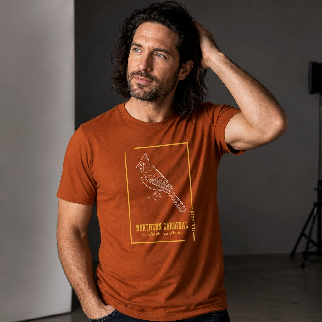 Man wearing an autumn orange Bella Canvas 3001 t-shirt with a vintage white line art northern cardinal illustration framed by minimalist golden borders and antique botanical typography, perfect for birders, naturalists, and wildlife art lovers, studio setting, by Crossroads Dandelion