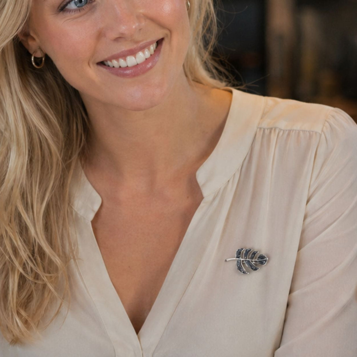 Young blonde woman wearing leaf brooch in coffee shop conversation, by Crossroads Dandelion