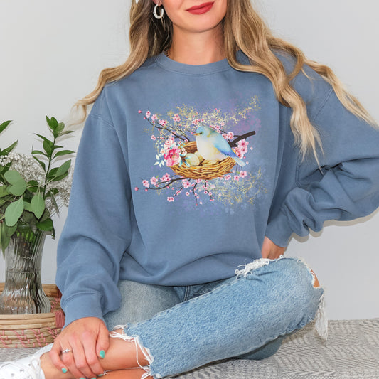 Person wearing a blue(blue jean) sweatshirt with a bird and nest design, sitting on a couch.
