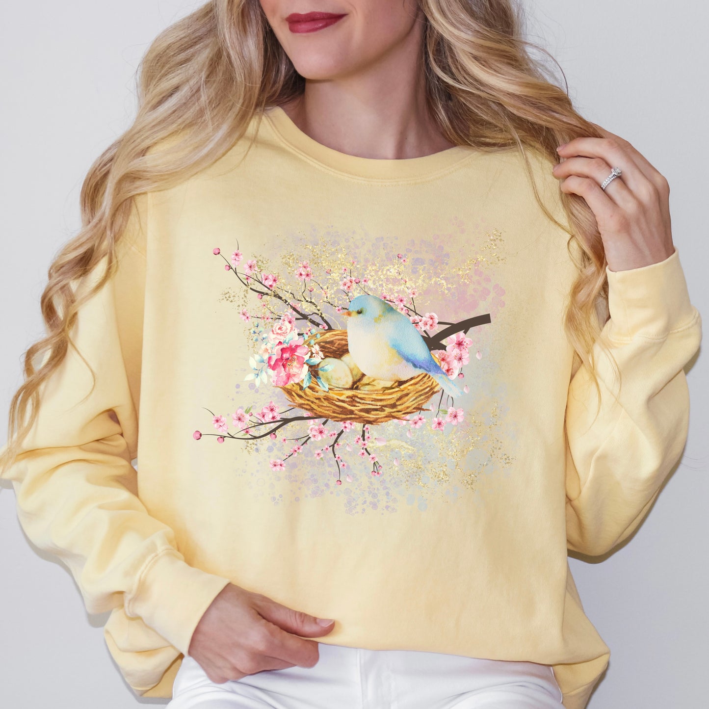 Person wearing a yellow sweatshirt with a bird and nest design on a light gray background