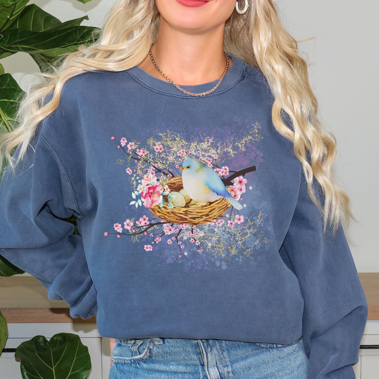 Person wearing a blue (blue jean color) sweatshirt with a bird and nest design.