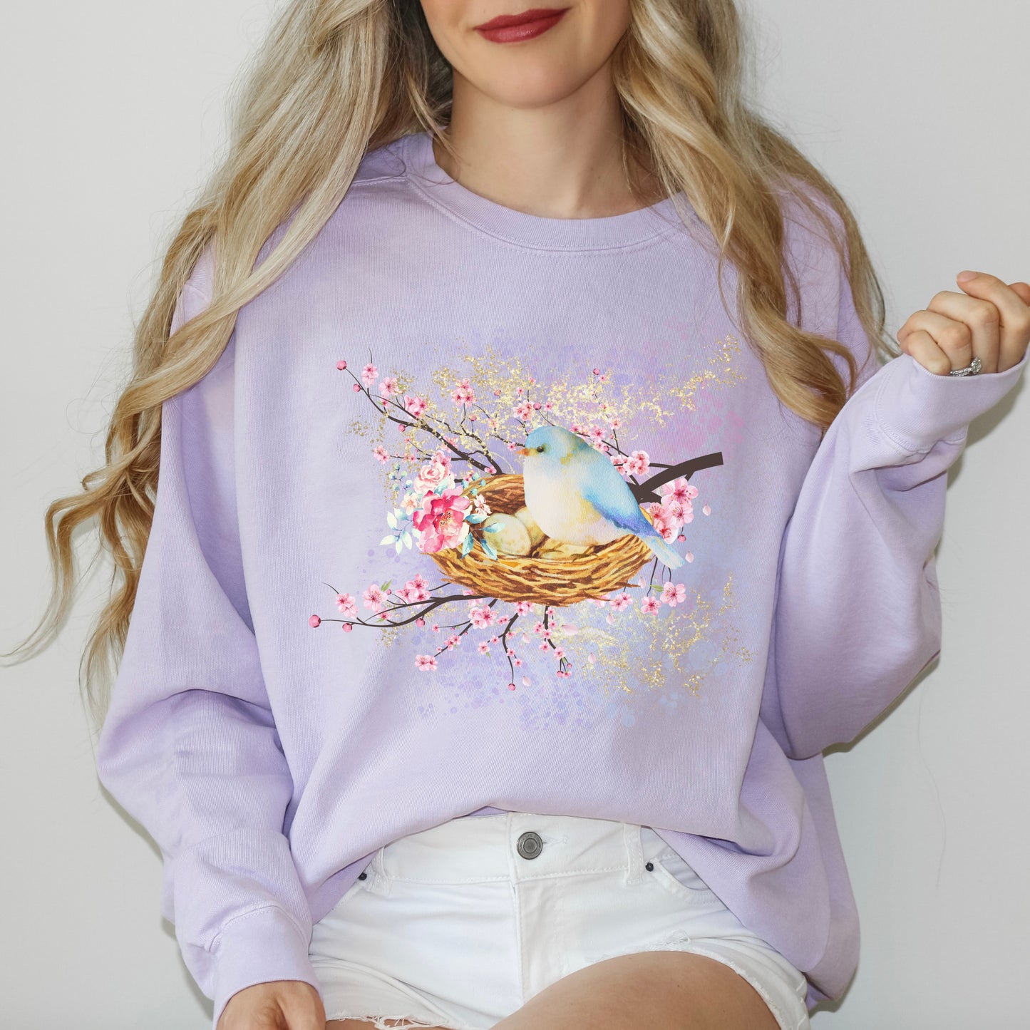 Person wearing a lavender(orchid) sweatshirt with a bird and nest design on a plain background
