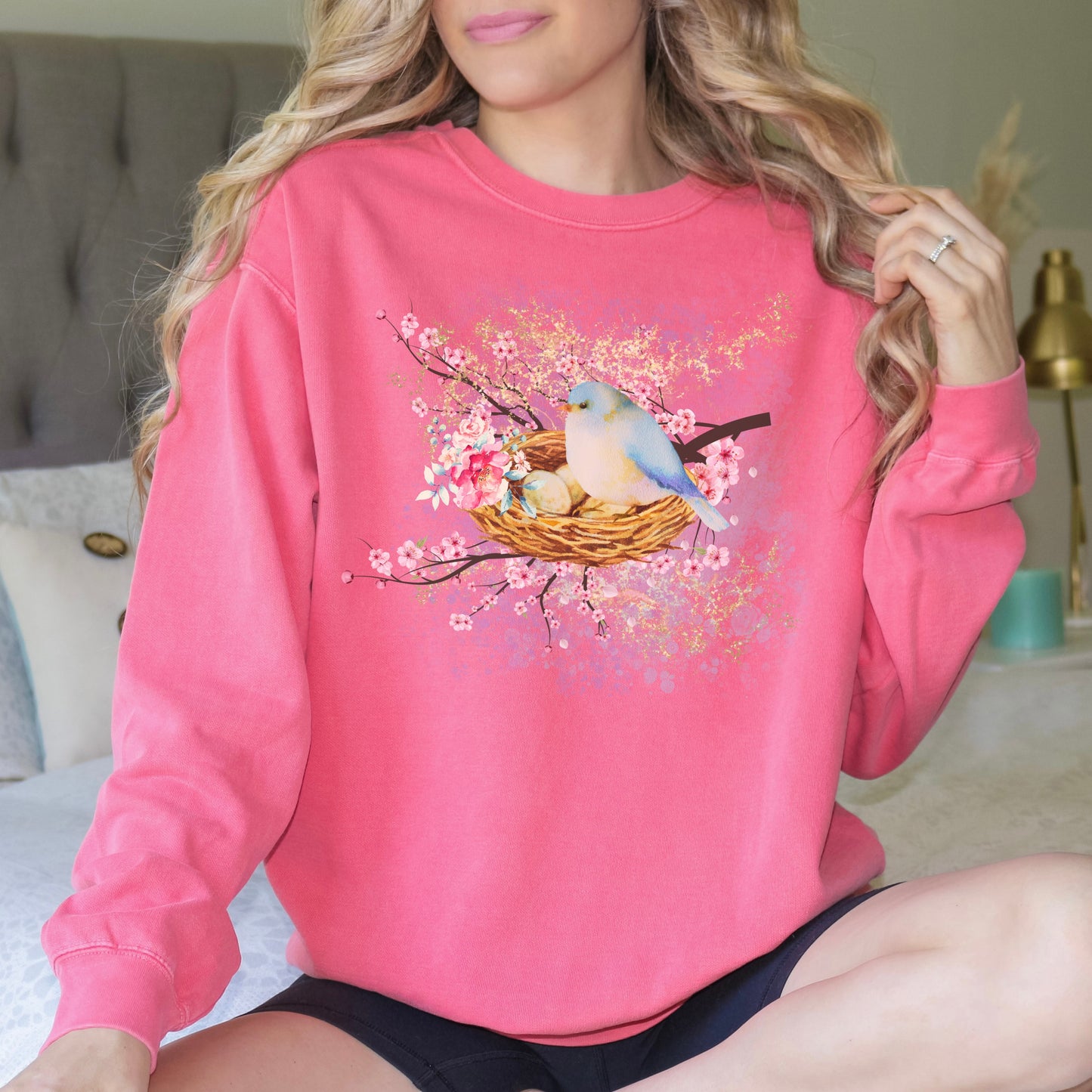 Person wearing a watermelon pink sweatshirt with a bird and nest design.