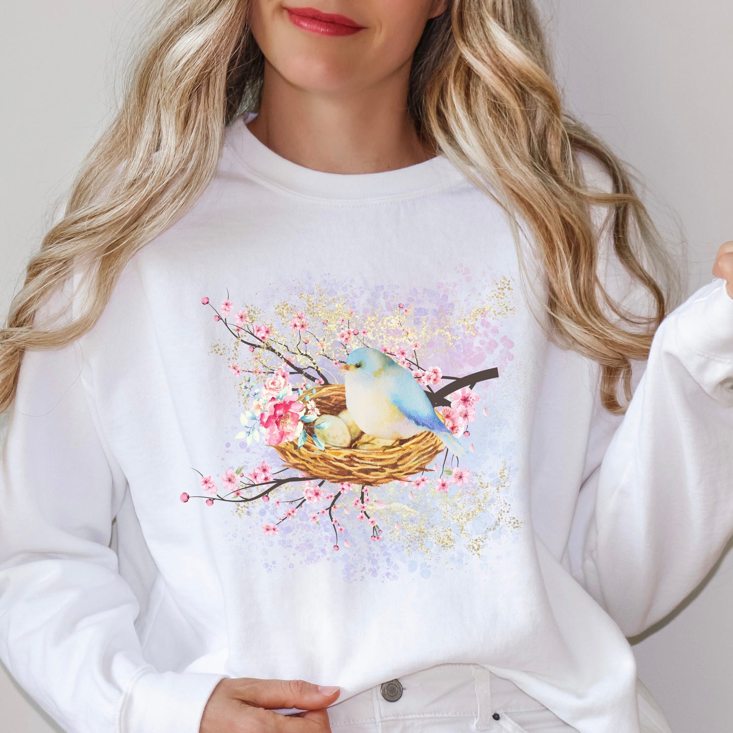White sweatshirt with a bird and nest design, worn by a person with blonde hair.