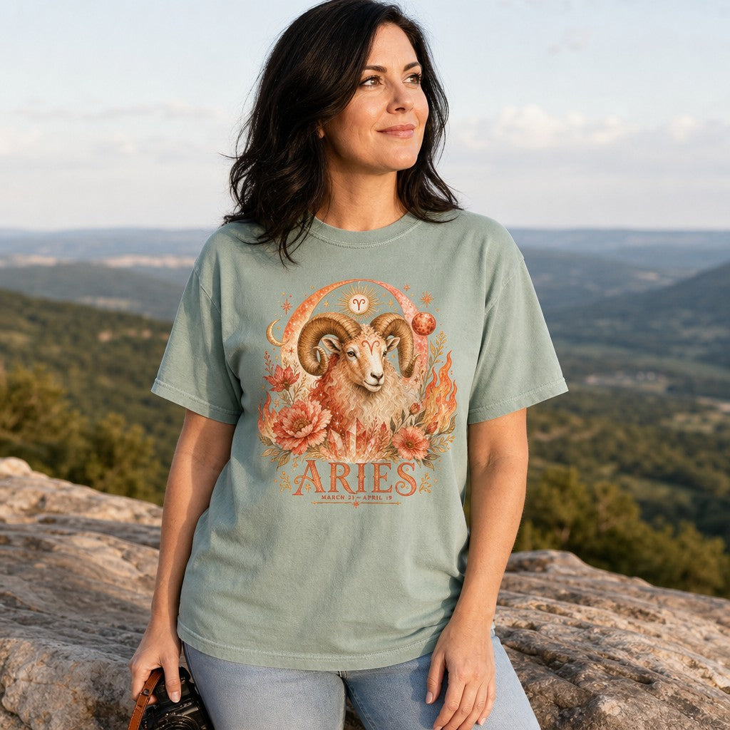 Woman wearing a bay Comfort Colors 1717 t-shirt with a vivid boho Aries ram design surrounded by fiery florals, cosmic moons, glowing crystals, and stars, standing on a mountain overlook, mystical astrology gift for women, by Crossroads Dandelion