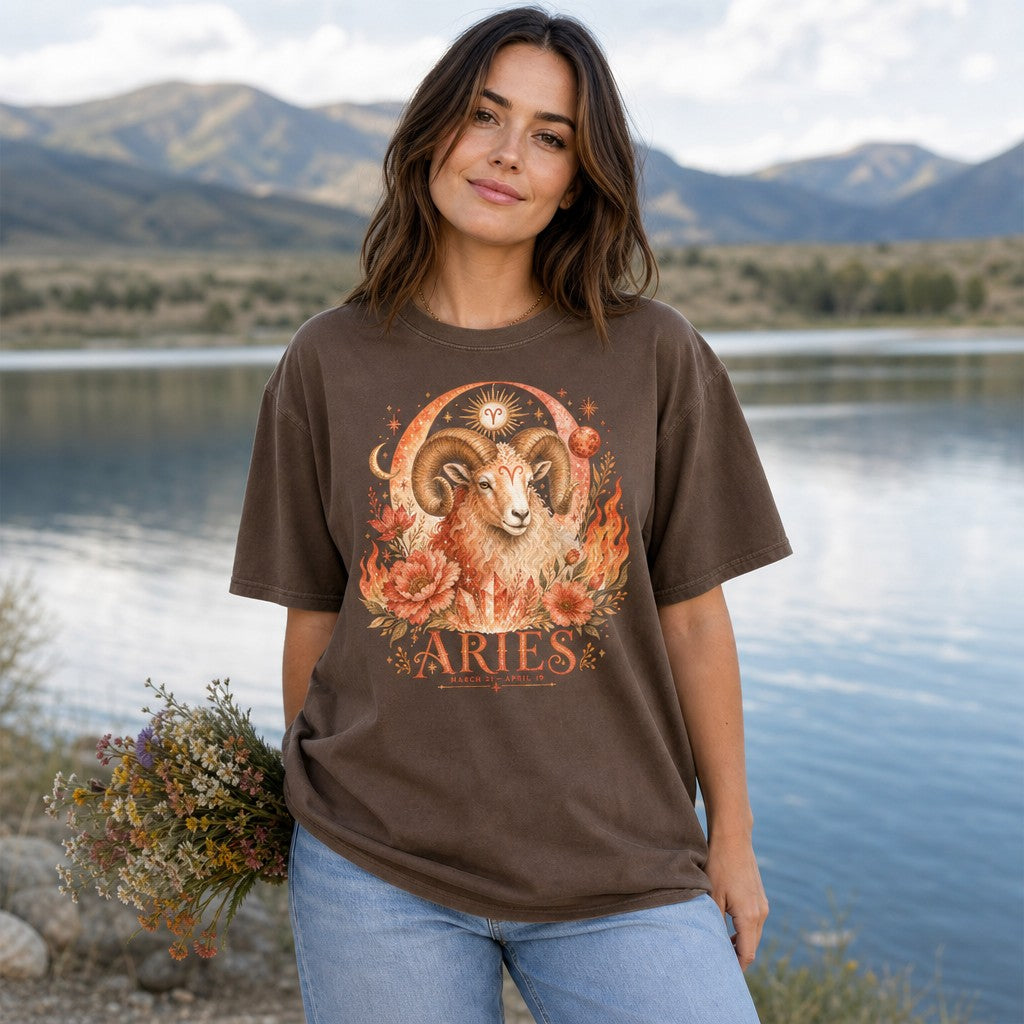 Woman in espresso Comfort Colors 1717 t-shirt featuring a vivid boho Aries ram design with fiery florals, cosmic moons, glowing crystals, and stars in warm hues, standing by a serene mountain lake, astrology lovers, by Crossroads Dandelion