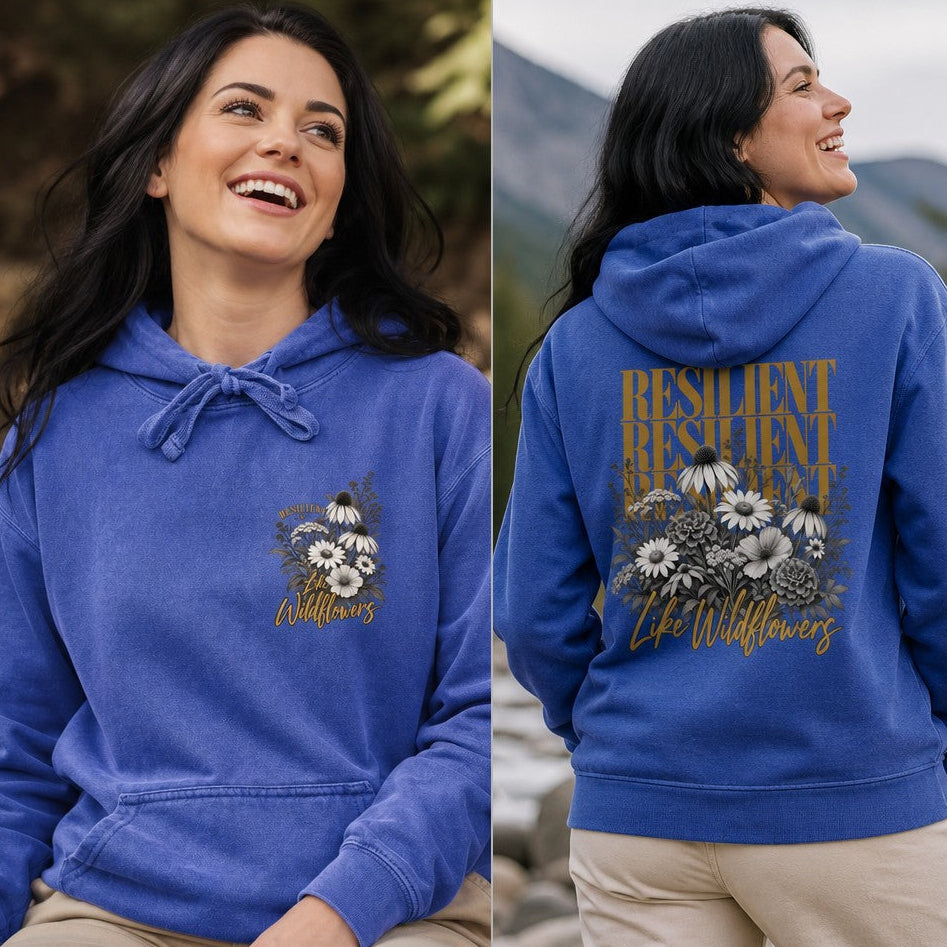 Woman wearing a flo blue hoodie with a boho floral design featuring daisies and the words 'Resilient Life Wildflowers', mountain lake background, perfect for nature lovers and women who appreciate inspiring botanical prints, by Crossroads Dandelion