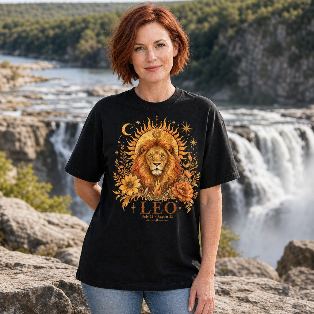 Woman wearing black Comfort Colors 1717 t-shirt with mystical boho Leo lion portrait, crowned by a blazing sun and Leo symbol, surrounded by celestial stars, moons, and gold-orange watercolor sunflowers and peonies, standing by a scenic waterfall; perfect for astrology and zodiac lovers, by Crossroads Dandelion
