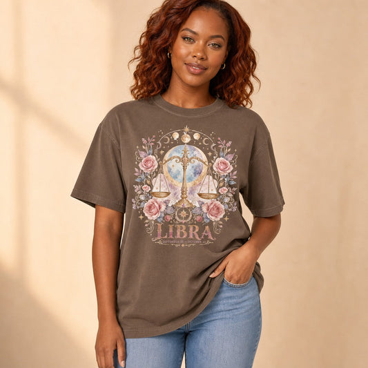 Woman wearing an espresso Comfort Colors 1717 t-shirt with a boho watercolor Libra scales illustration surrounded by dreamy pink roses, crescent moons, gold stars, and cosmic accents, designed for zodiac and astrology lovers, by Crossroads Dandelion