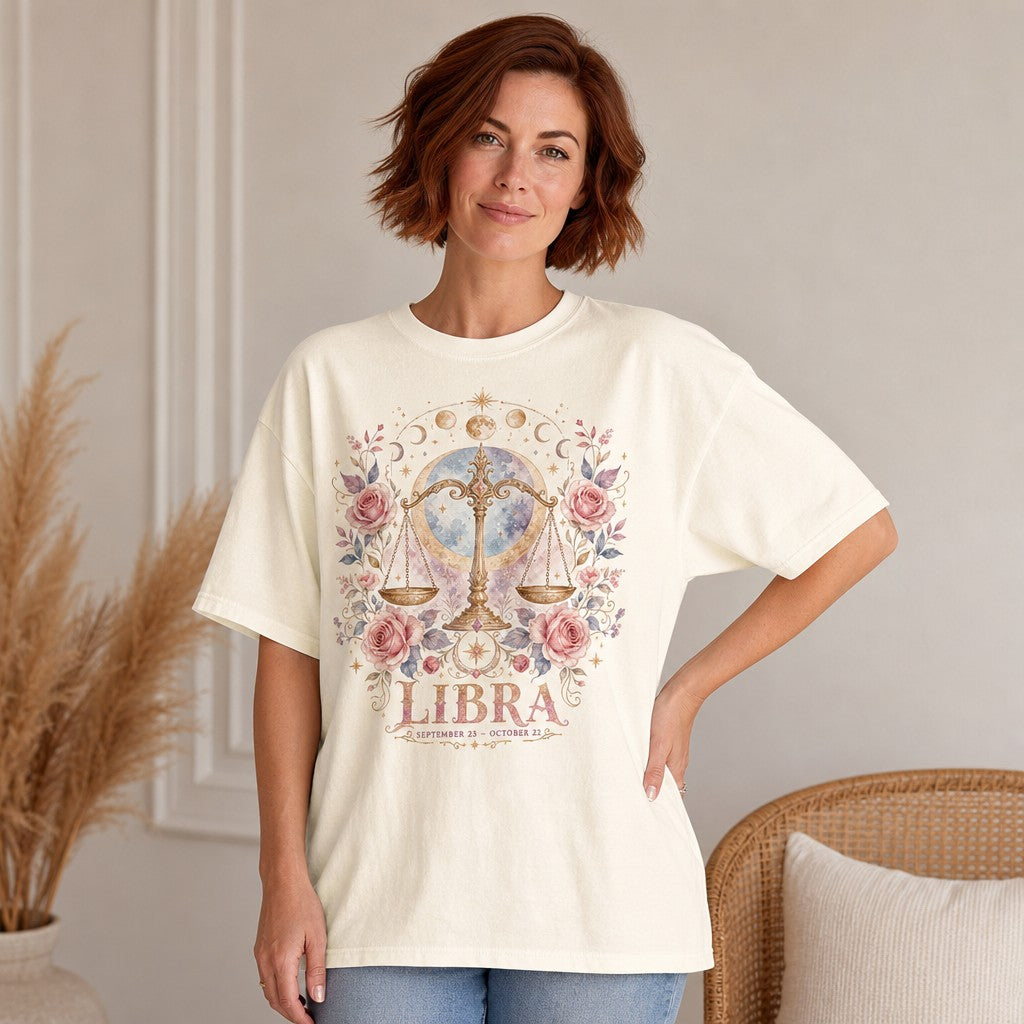 Woman wearing an ivory Comfort Colors t-shirt with a boho watercolor Libra scales and pink roses design, celestial and astrological accents, cozy indoor setting, ideal for zodiac lovers and free spirits, by Crossroads Dandelion