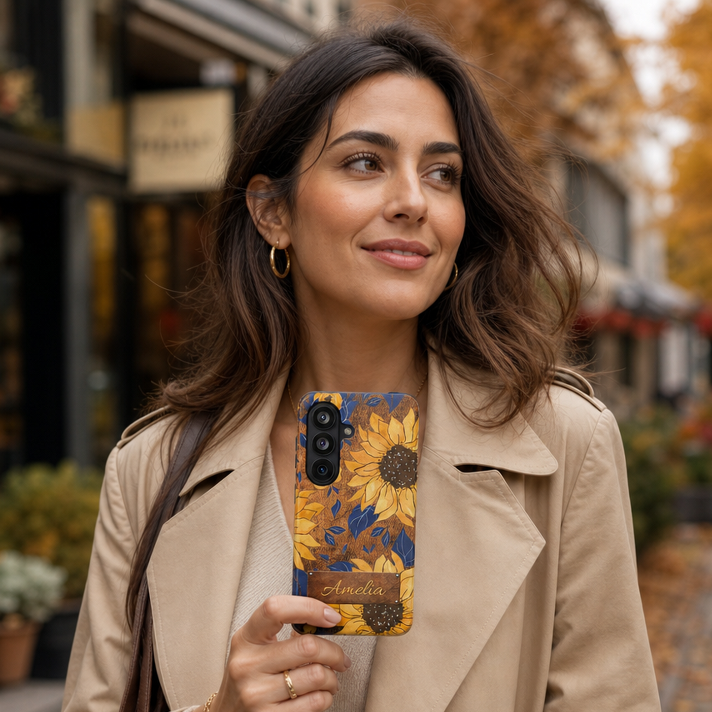 Fashionable woman holding a boho sunflower phone case with autumn floral pattern in yellow and brown, walking through a charming downtown street, designed for women who love seasonal botanical styles, by Crossroads Dandelion