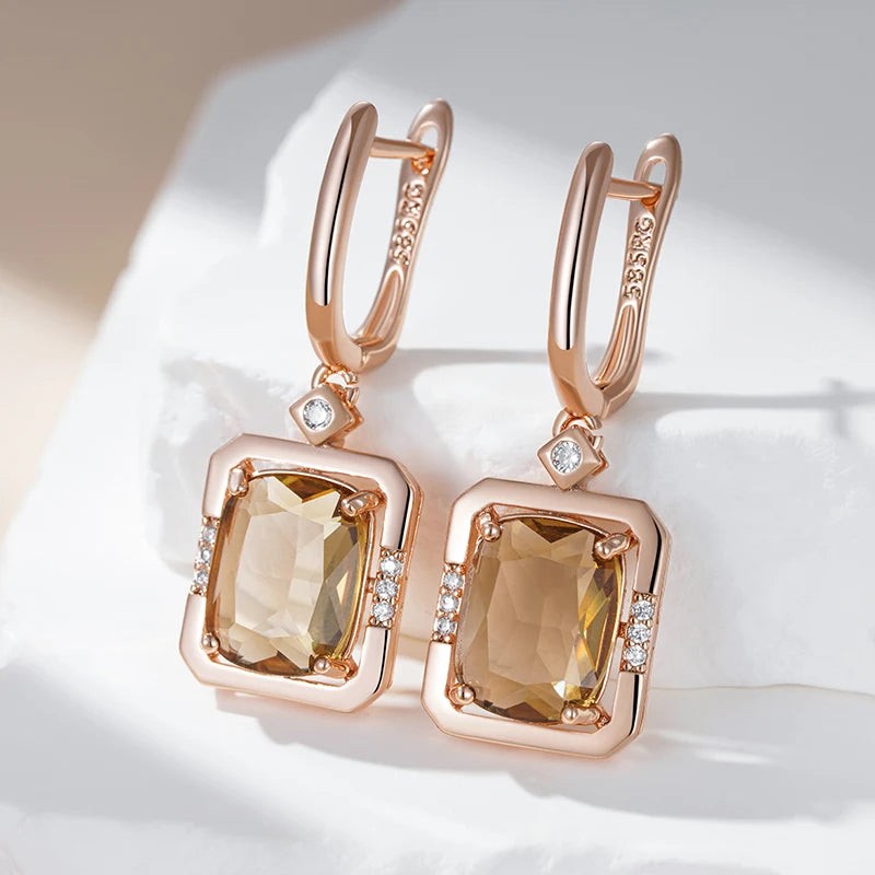 Rose gold champagne square drop earrings resting on white stone in soft light