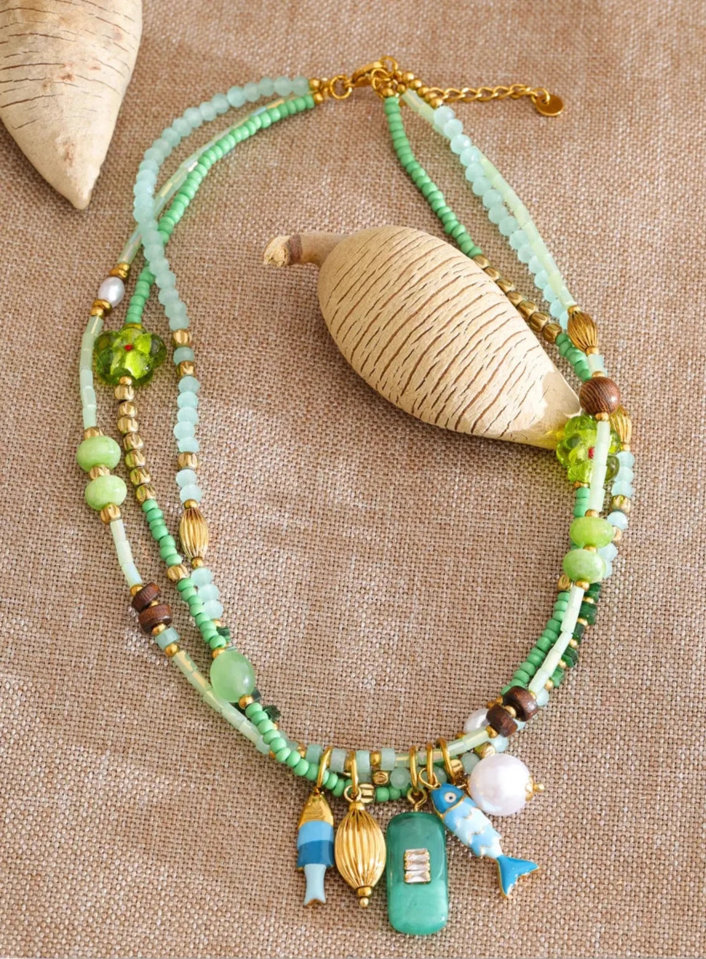 Multistrand beaded necklace with fish charms on a textured beige surface by Crossroads Dandelion