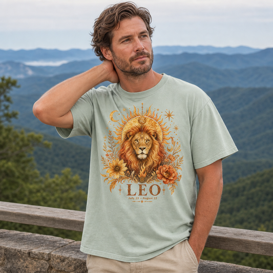 Man wearing Comfort Colors 1717 t-shirt in bay green with vintage ethereal Leo zodiac lion design featuring sun, moon, stars, and autumnal flowers, mystical astrology print for zodiac enthusiasts, mountain overlook setting, by Crossroads Dandelion