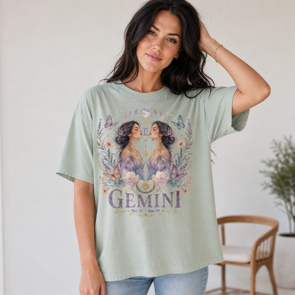 Woman wearing a Comfort Colors 1717 t-shirt in bay green with a whimsical boho Gemini design featuring watercolor twin women, pastel butterflies, flowers, and celestial accents, perfect for astrology and zodiac lovers, indoor setting, by Crossroads Dandelion