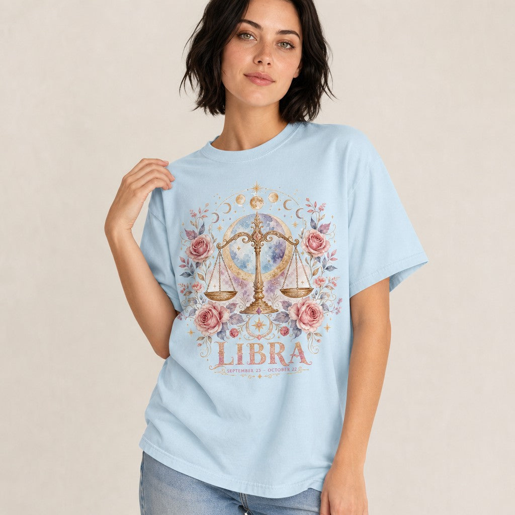 Woman wearing chambray Comfort Colors 1717 t-shirt with a boho watercolor Libra scales design, surrounded by pink roses, golden stars, crescent moons, and celestial accents, mystical astrology t-shirt for zodiac lovers and free spirits, by Crossroads Dandelion