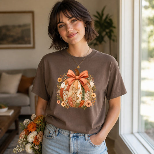 Woman wearing an espresso Comfort Colors 1717 t-shirt featuring a cottagecore patchwork pumpkin with vintage floral fabrics, a soft bow, whimsical ghosts, and botanical blooms in a cozy autumn palette, perfect for handmade artistry and nostalgic fall style, by Crossroads Dandelion