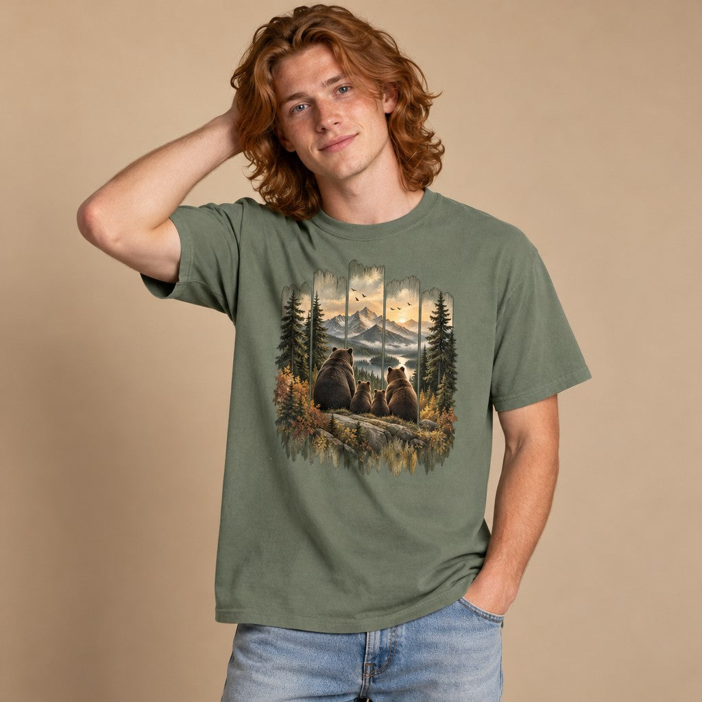 Man wearing moss green Comfort Colors® 1717 t-shirt featuring a vintage-style painted scene with a brown bear family overlooking mountain sunset, winding river, and autumn pines in distressed wood-panel frame, perfect for hikers, campers, and wildlife lovers, by Crossroads Dandelion