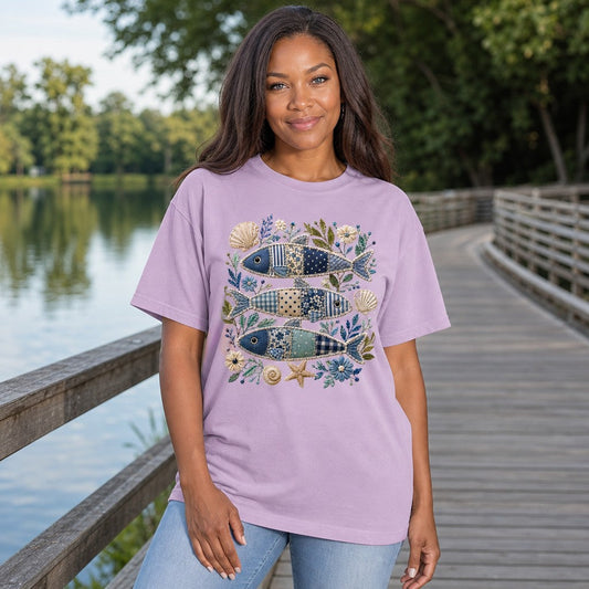 Woman in orchid Comfort Colors 1717 t-shirt with a whimsical patchwork sardine fish and seashells floral folk art design, cottagecore and coastal vintage style, relaxing lakeside, for creative nature-loving women, by Crossroads Dandelion