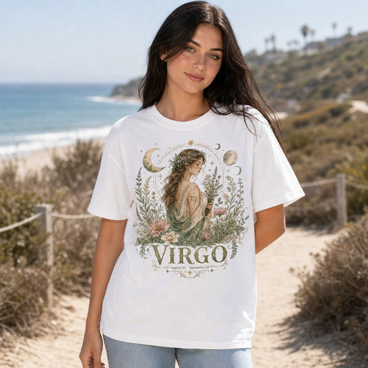 Woman wearing a white Comfort Colors 1717 t-shirt with a whimsical boho celestial Virgo goddess and wildflowers design, moons and stars, in soft earth tones, standing by the beach, astrology lovers and spiritual women, by Crossroads Dandelion