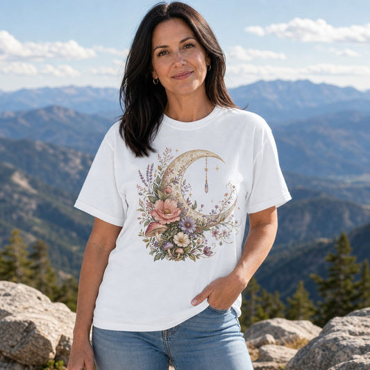 Woman wearing white Comfort Colors 1717 t-shirt with cottagecore watercolor crescent moon, wildflowers, whimsical mushrooms, and lavender design, standing in mountains, dreamy celestial vibe, for nature lovers and botanical art fans, by Crossroads Dandelion