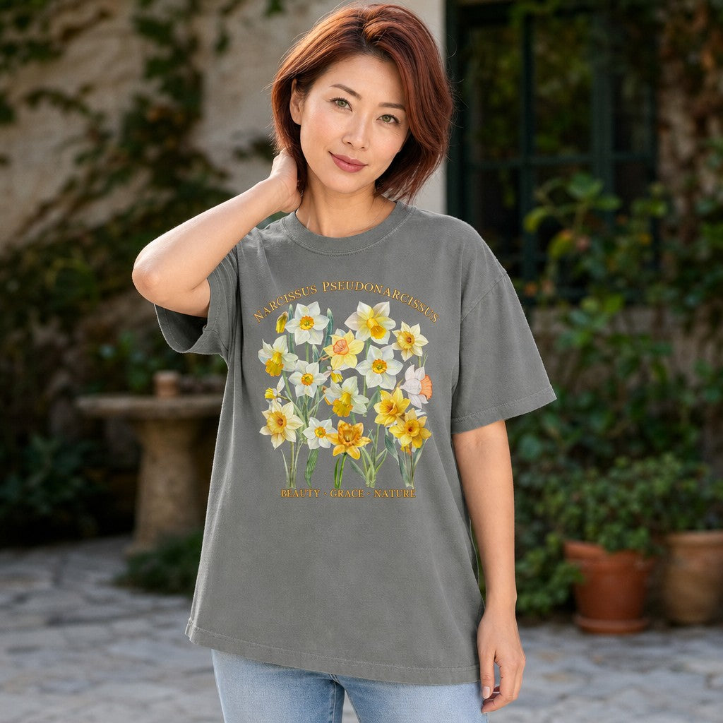 Woman in grey Comfort Colors 1717 t-shirt featuring a vintage botanical watercolor illustration of Narcissus pseudonarcissus daffodil flowers with gold labeling, cottagecore floral design, garden courtyard setting, ideal for floral enthusiasts, by Crossroads Dandelion