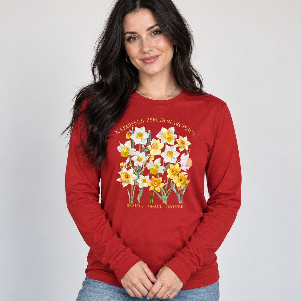 Woman wearing a red Bella Canvas 3501 long sleeve shirt featuring a cottagecore watercolor daffodil botanical specimen design with vintage Latin script, ideal for plant lovers, gardeners, and creative souls, by Crossroads Dandelion