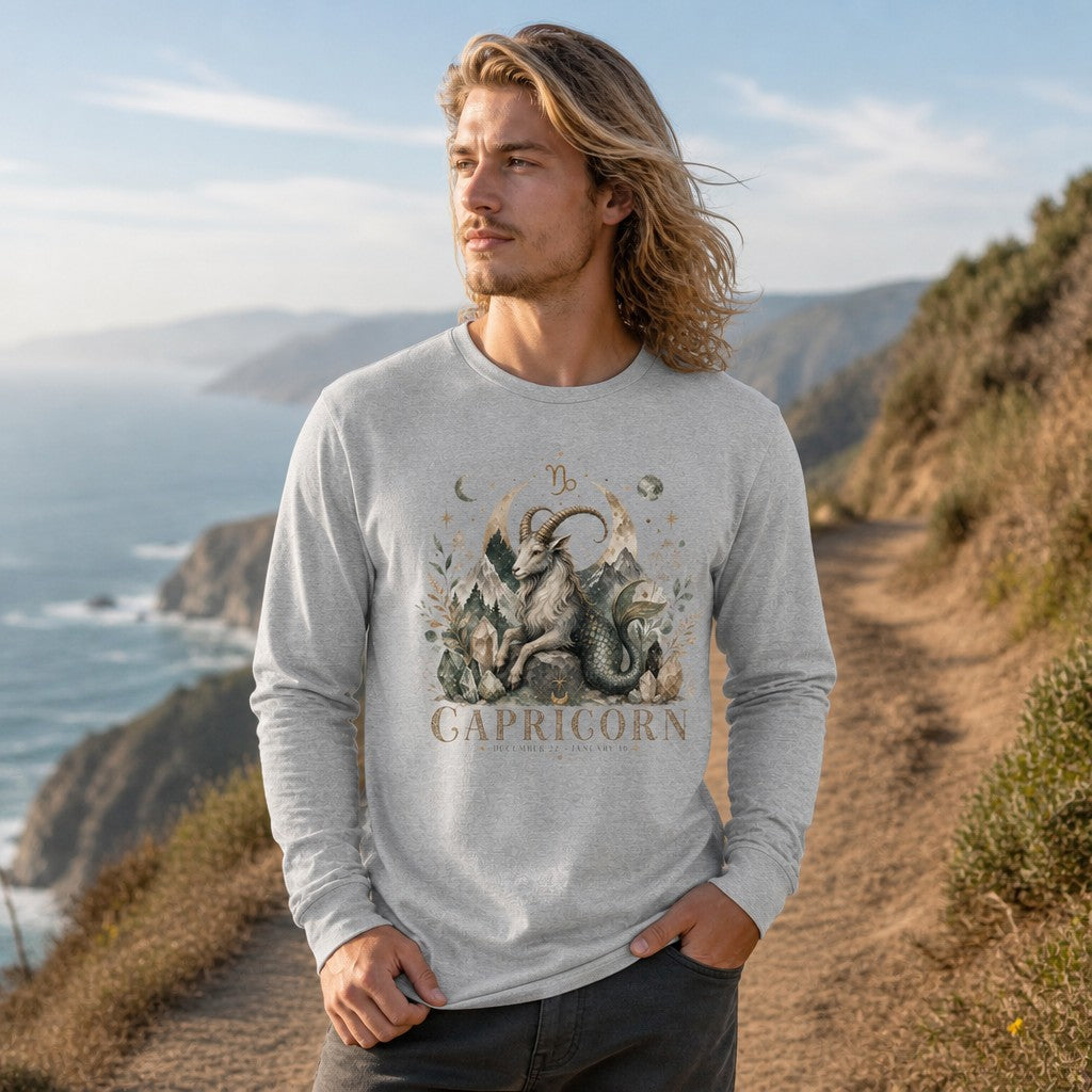 Man in athletic heather long sleeve Bella Canvas 3501 featuring a watercolor Capricorn sea-goat design with vintage zodiac symbolism, moon phases, botanicals, and crystalline mountains, standing on a coastal cliff trail, ideal for astrology lovers and garden dreamers, by Crossroads Dandelion