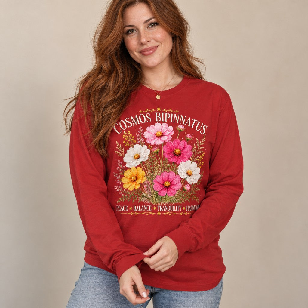 Woman in red Bella Canvas 3501 long sleeve featuring a vintage-inspired watercolor botanical design of Cosmos bipinnatus flowers in soft pink, white, and yellow hues with celestial accents, perfect for cottagecore fans and October birthdays, by Crossroads Dandelion