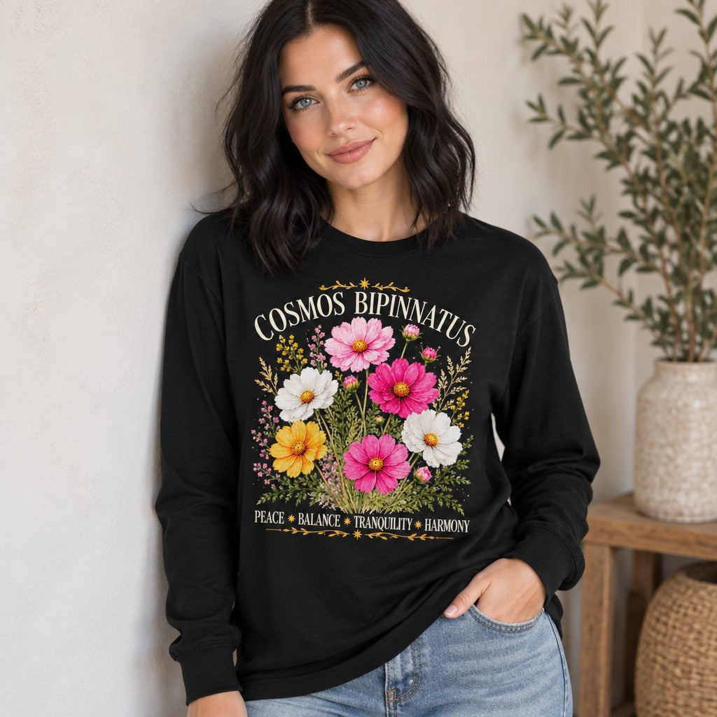 Woman wearing a black Bella Canvas 3501 long sleeve shirt featuring a vintage watercolor bouquet of pink, white, and yellow cosmos bipinnatus with golden celestial accents and botanical foliage, perfect for cottagecore lovers and October birthdays, indoors, women's cozy floral apparel, by Crossroads Dandelion