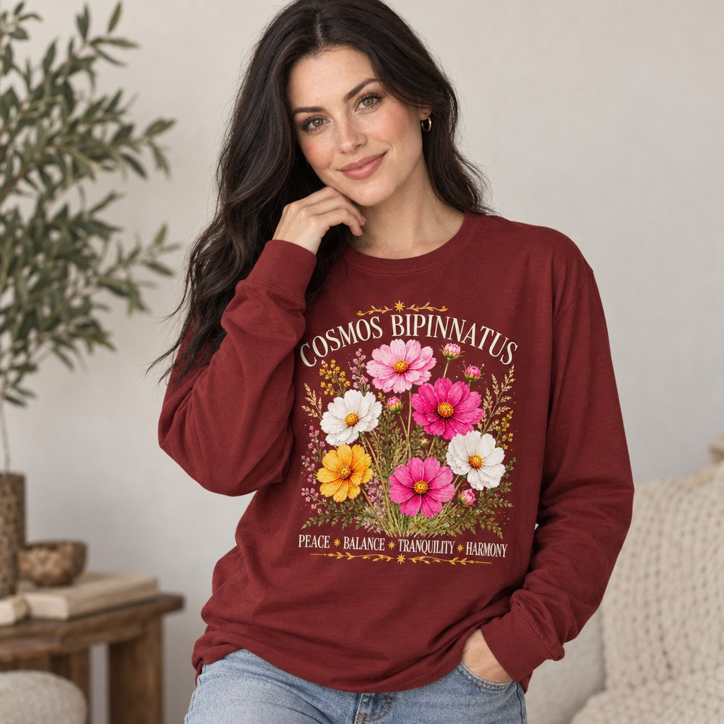 Woman in a cardinal red Bella Canvas 3501 long sleeve featuring a vintage watercolor bouquet of cosmos bipinnatus blooms with celestial accents and delicate foliage, cottagecore botanical illustration for peaceful living, perfect for October birthdays and floral lovers, cozy indoor setting, by Crossroads Dandelion