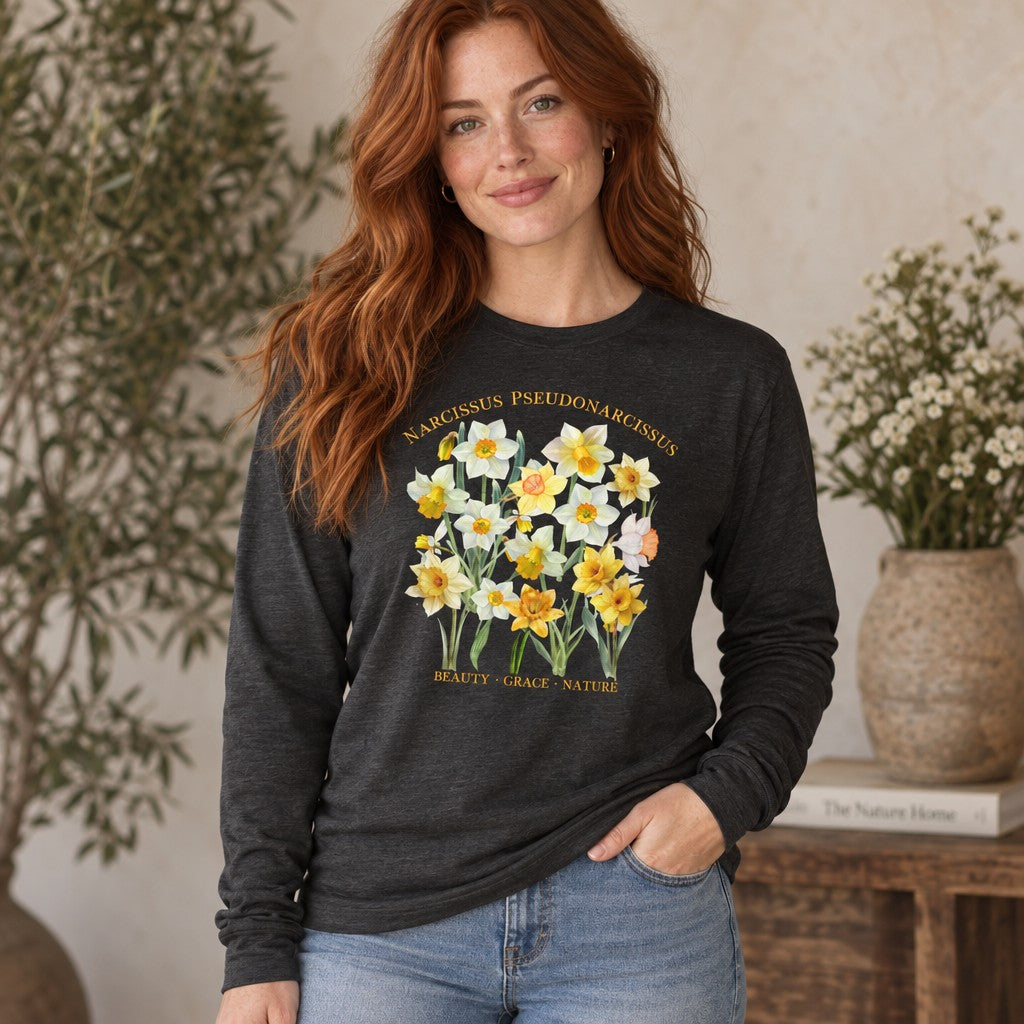 Woman with red hair wearing a dark grey heather Bella Canvas 3501 long sleeve shirt featuring vintage watercolor daffodil blooms arranged as a botanical specimen with Latin script, cozy indoor setting with cottagecore and botanical appeal, ideal for creative women and nature-inspired plant lovers, by Crossroads Dandelion