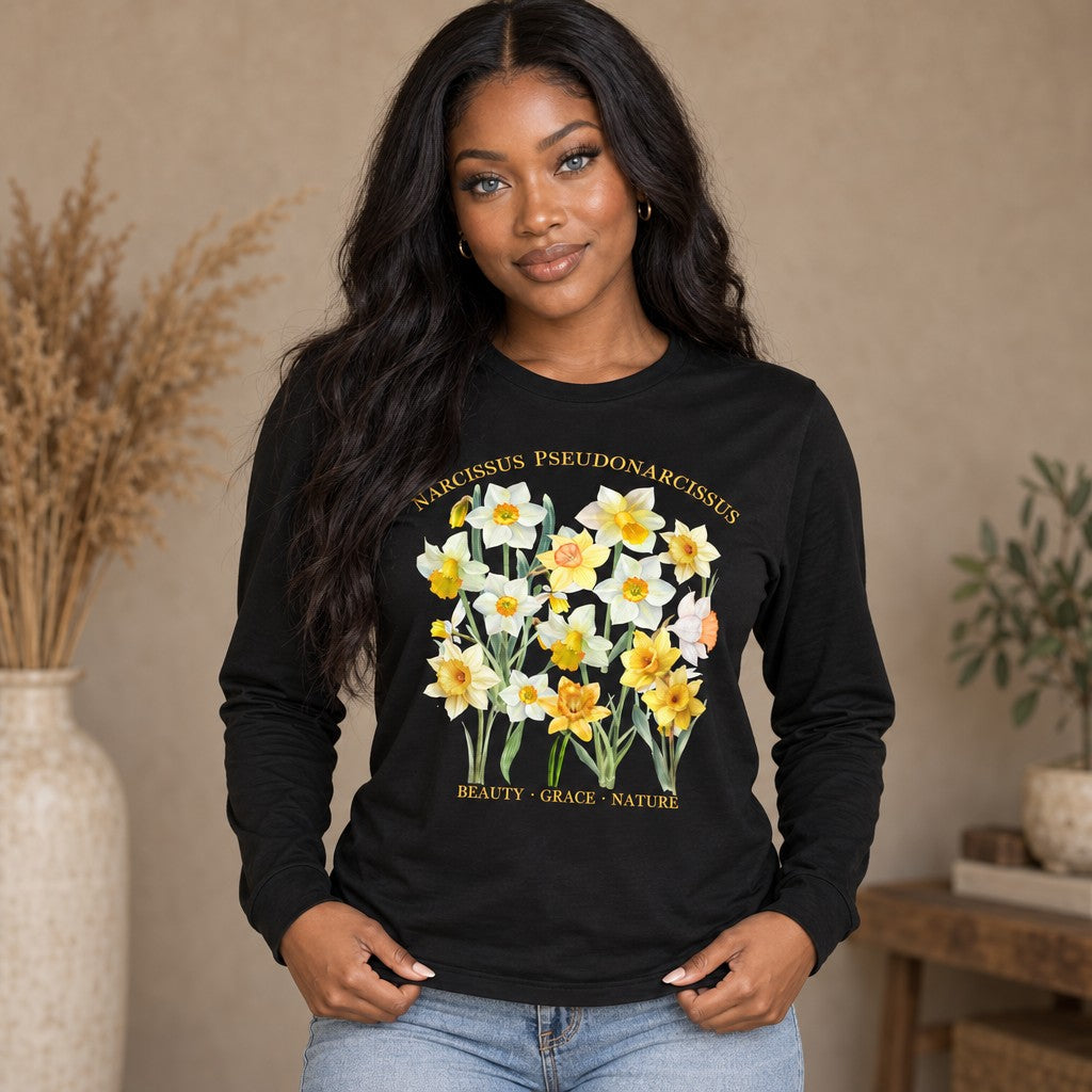 Woman wearing a black long sleeve Bella Canvas shirt with a cottagecore watercolor daffodil botanical design and elegant Latin lettering, styled indoors for creative plant lovers and floral enthusiasts, by Crossroads Dandelion