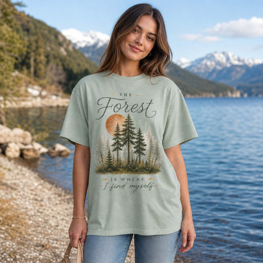Woman wearing bay Comfort Colors 1717 t-shirt featuring a hand-painted woodland scene with pine trees, golden full moon, and mossy undergrowth in a vintage cottagecore style, standing by a mountain lake, nature and introspective design for women and nature lovers, by Crossroads Dandelion