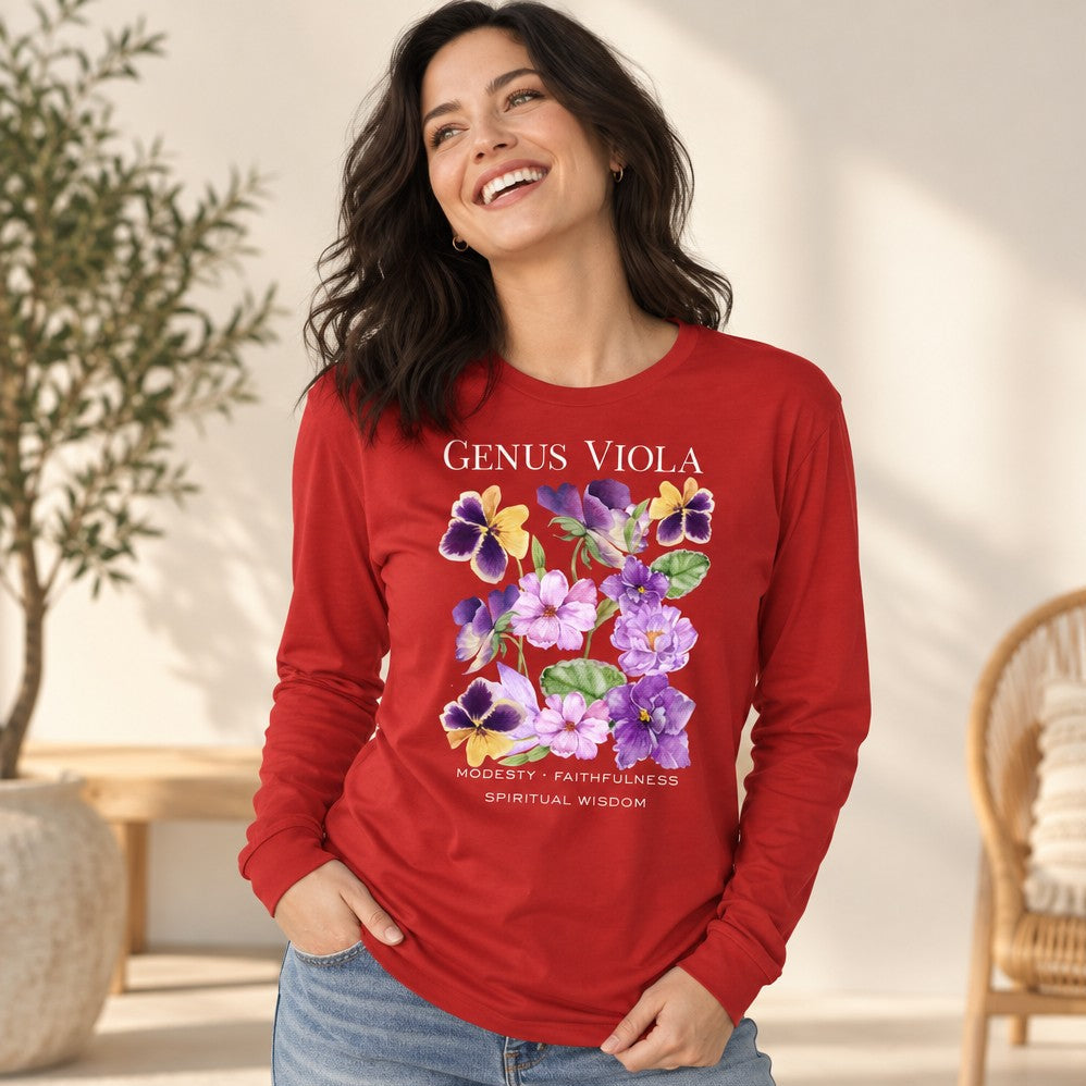 Woman wearing a red Bella Canvas 3501 long sleeve shirt featuring a cottagecore watercolor design of violets, pansies, and heart-shaped leaves with botanical symbolism for modesty, faithfulness, and spiritual wisdom, vintage nature journal aesthetic, perfect for botanical art lovers, by Crossroads Dandelion