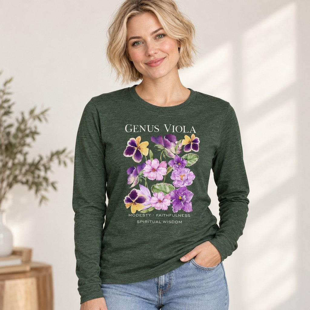 Blonde woman wearing a heather forest Bella Canvas 3501 long sleeve shirt featuring a cottagecore watercolor design of lush violets, pansies, and botanical symbolism for modesty, faithfulness, and spiritual wisdom, vintage nature journal style, perfect for botanical art enthusiasts, by Crossroads Dandelion