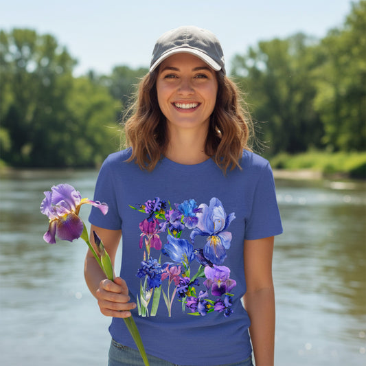 Woman wearing a heather true royal tee with a beautiful iris flowers design. Woman is holding an iris flower in front of a lake.