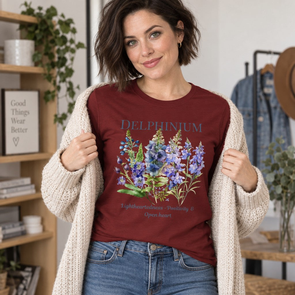 Woman wearing a cardinal red Bella Canvas 3501 long sleeve shirt featuring a vintage watercolor larkspur floral design with cottagecore vibes, set in a cozy modern home, perfect for plant lovers and botanical enthusiasts, by Crossroads Dandelion